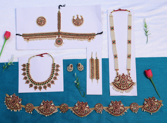 Complete Bharatanatyam jewellery set laid out on blue fabric, featuring red and green kemp stones and pearls