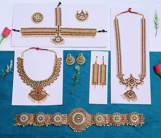 Full Arangetram Bharatanatyam temple jewellery set with Kemp stones, including haram, choker, jhumkas, vanki, oddiyanam, and headpiece arranged on a blue and white background.