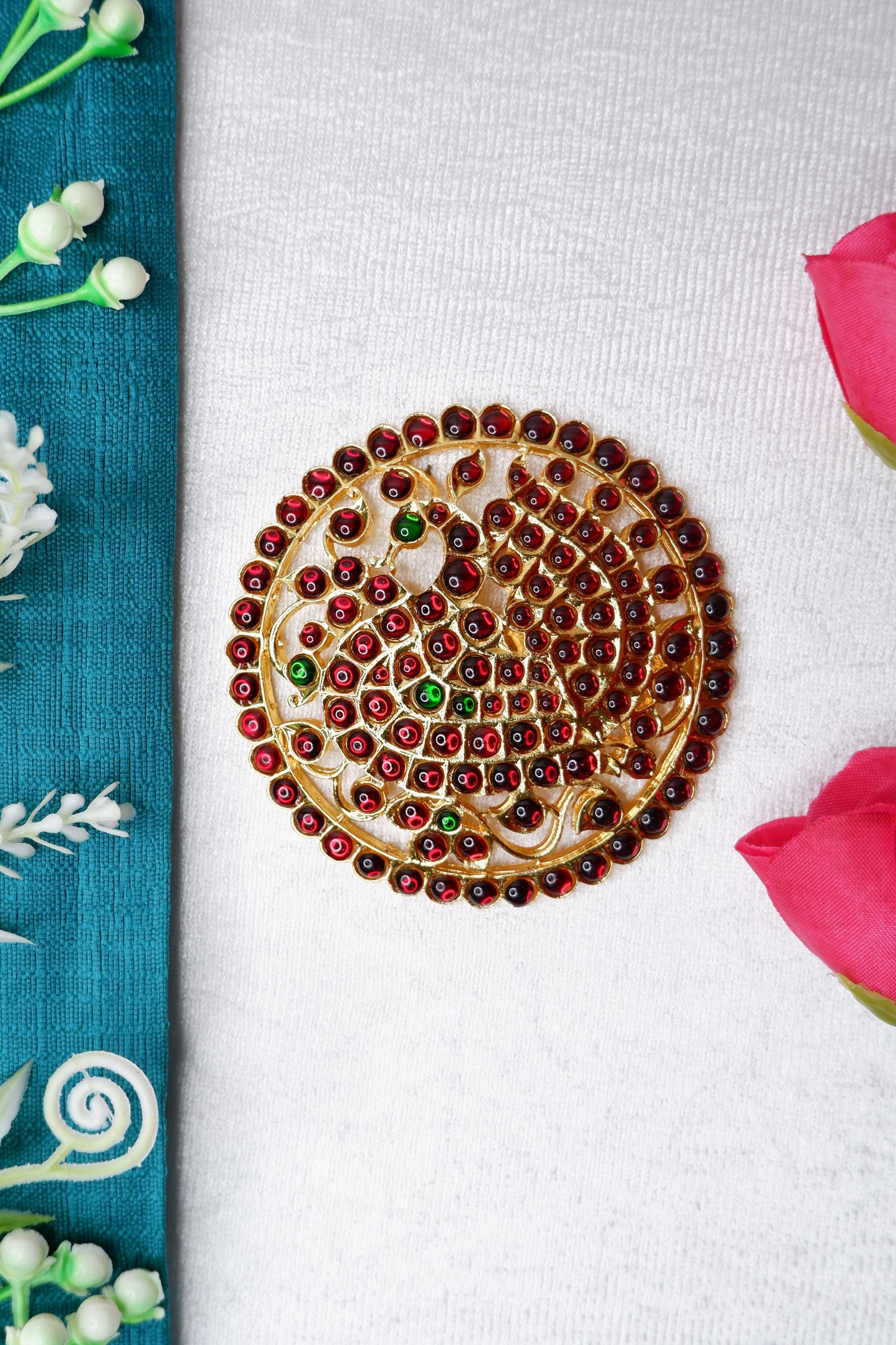 A Bharatanatyam/Kuchipudi dancer with a circular ragaadi rakodi hair ornament placed at the center of the braided bun, decorated with gold-toned metal, gemstones, and floral elements, complementing the classical temple jewelry and stage makeup
